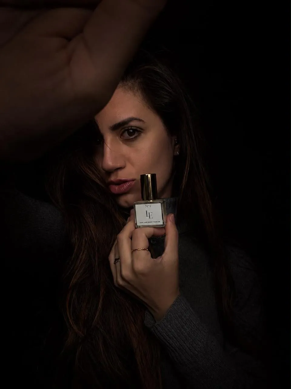 Retrato em luz baixa de uma mulher segurando o frasco LE E'ssence Nº1 junto ao rosto